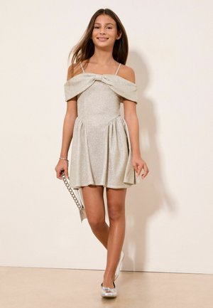 Tüdruk kõnnib säravas hõbedases õlglõhnavas kleidis, millel on õhukesed rihmad, hoides hõbedast käekotti ja kandes hõbedasi kingi.