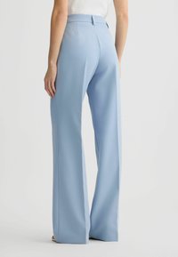 Helleblaue maßgeschneiderte Hose mit hoher Taille, weitem Bein, glatter Textur und dezenten Falten auf der Rückseite.