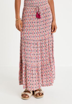 Langer gemusterter Rock mit rosa, orangefarbenen und schwarzen Rautenmuster, verziert mit Quasten an der Taille, getragen mit beigen Sandalen mit Schnalle.