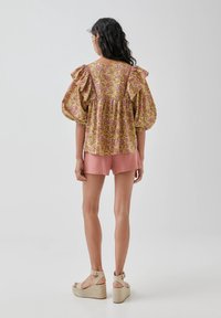 Blouse florale colorée avec des manches bouffantes, assortie à un short rose et des sandales à plateforme. La blouse présente des motifs complexes et une coupe ample.