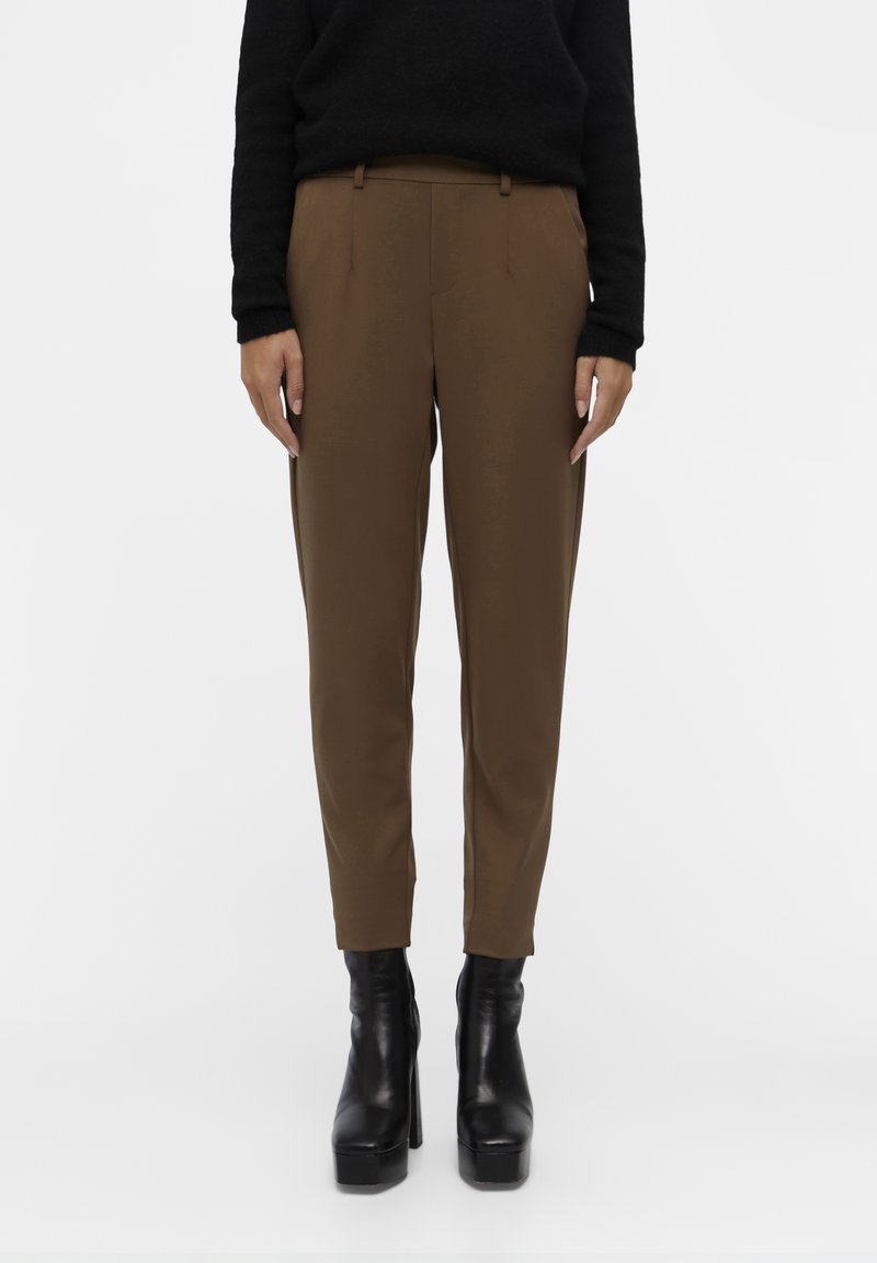 Brune skreddersydde bukser med en jevn tekstur, med frontlommer og en smalere design. Kombinert med svarte platåsko.