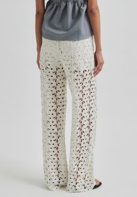 Pantaloni in pizzo all'uncinetto in bianco avorio, con design a gamba larga, caratterizzati da motivi floreali e una lavorazione a trama aperta, abbinati a un top grigio.