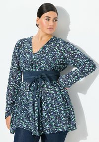 Blomstret bluse i mørkeblå med grønne og hvide detaljer, lange ærmer, V-udskæring og en bundet taljedetalje.