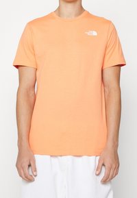 Pomarańczowa bawełniana koszulka z krótkim rękawem z białym logo po lewej stronie klatki piersiowej. Klasyczny okrągły dekolt i standardowy krój. Gładka tekstura.