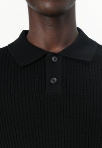 Μαύρο ριγέ πόλο πουκάμισο με γιακά, δύο κουμπιά και υφή υφάσματος. Λείος φινίρισμα, μινιμαλιστικός σχεδιασμός και χωρίς ορατά μοτίβα.