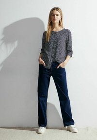 Camicia a maniche lunghe con bottoni di colore blu navy con motivo astratto bianco, abbinata a jeans in denim scuro e sneakers bianche.