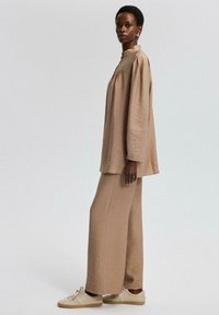 Beige two-piece outfit featuring a loose long-sleeve top with a high collar and wide-legged trousers, made from textured fabric.