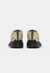 Scarpe da trail beige con suola nera e dettagli rosa, tomaia testurizzata e collo imbottito con un linguetta verticale a strisce.