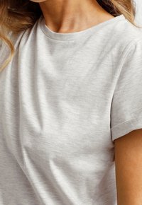 Jasnoszara dzianinowa koszulka z okrągłym dekoltem i podwiniętymi krótkimi rękawami. Materiał wydaje się miękki, ma subtelną teksturę i lekki układ.