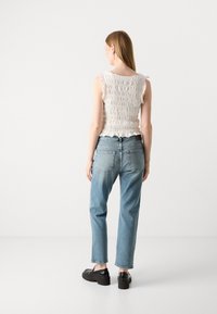 Biały top z falbaniastymi rękawami, zestawiony z jasnoniebieskimi dżinsami o prostym kroju i czarnymi butami na platformie. Widok z tyłu o gładkiej fakturze.