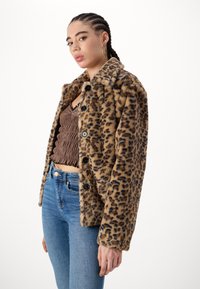 Sako z imitace kůže s leopardím potiskem, s předním zapínáním na knoflíky, širokým límcem a volným střihem. Nosené přes hnědý top s nařasením a modré džínsy.
