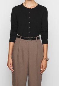 Cardigan nero con bottoni in morbido tessuto, con maniche lunghe e scollatura rotonda, abbinato a pantaloni marroni a vita alta e una cintura nera.