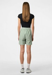 Groene en witte gestreepte shorts met een elastieken tailleband, van achteren weergegeven, gecombineerd met een zwarte aansluitende top en witte sneakers.