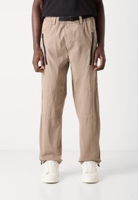 Beige cargo pants made of lightweight fabric, featuring side zip pockets, elastic waistband, and tapered legs with hem zippers.