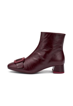 Stivaletti alla caviglia in pelle bordeaux con punta affusolata, tacco basso a blocco e una grande fibbia decorativa sul lato esterno. Texture liscia.
