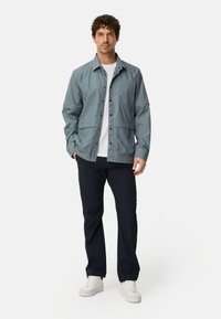 Lyseblå skjortejakke med to forlommer, kombineret med navy bukser og hvide sneakers. Glat stoftekstur, afslappet design.