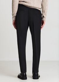 Pantaloni neri su misura con design a gamba dritta, due tasche posteriori e una texture liscia. Indossati con un maglione chiaro a trecce e scarpe nere.