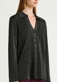 Maglia nera a maniche lunghe con leggera lucentezza. Presenta uno scollo a V, colletto e una patta con sei bottoni. Tessuto morbido con scintillii delicati.