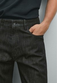 Dunkelblaue Denim-Jeans mit enganliegendem Schnitt, ausgestattet mit einer Fronttasche, subtiler Textur und einem einzelnen Knopfverschluss an der Taille.