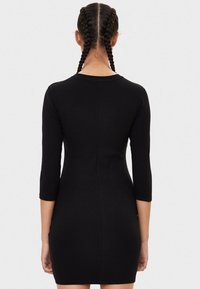 Svart ribbad klänning med trekvartslånga ärmar, figurnära silhuett och rund halsringning. Slät textur och mitt på låret längd.