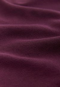 Mørkelilla stof med en tekstureret, strikket overflade, der har subtile folder og krøller, som antyder fleksibilitet og blødhed.