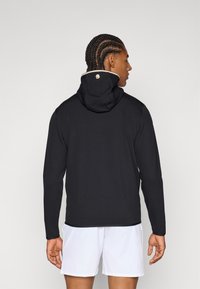 Svart hoodie med hög krage och dragsko, med en liten logga på baksidan. Slät tyg och långa ärmar med ribbad mudd.
