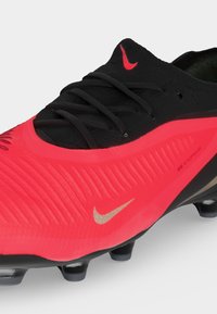 Κόκκινο και μαύρο ποδοσφαιρικό παπούτσι Nike με κορδόνια, λογότυπα Nike και υφή στο επάνω μέρος με την ένδειξη Nike Venomskin, ορατά τάπες στη σόλα.