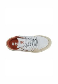 Zapatilla deportiva blanca con parte superior de piel lisa, acentos naranjas en el forro interior y el logo, y suela de goma beige. Presenta un sistema de cordones clásico.