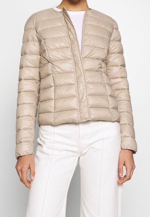 Veste matelassée beige, design matelassé avec des lignes horizontales étroites, devant sans fermeture éclair, tissu léger, associée à un pantalon blanc taille haute.