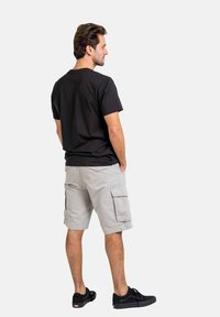 Schwarzes Baumwoll-T-Shirt mit Rundhalsausschnitt, kombiniert mit hellgrauen Cargo-Shorts mit Seitentaschen, getragen mit schwarzen Sneakers.