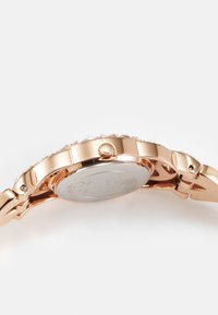 Roséguld klocka med en dekorativ bezel, rund urtavla och metallarmband. Har en sidokrona och slät baksida i silver.