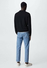 Pull noir à manches longues avec un ourlet côtelé, associé à un jean en denim bleu clair. Des baskets aux tons neutres complètent la tenue.