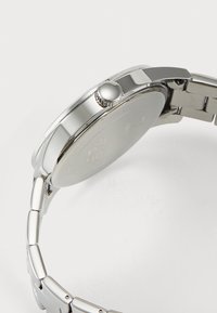 Reloj de acero inoxidable plateado con un diseño elegante, caja redondeada y detalle texturizado en la corona. La pulsera cuenta con eslabones pulidos.