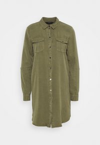 Robe chemise vert olive à manches longues avec fermeture à boutons sur le devant et deux poches à rabat poitrine sur fond blanc.
