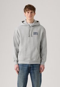 Sweatshirt gris avec capuche, présentant une poche avant et un logo bleu "LEVI'S". Porté avec un jean bleu, il a une coupe décontractée et une texture douce.