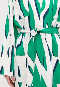 Green and white patterned wrap dress, featuring a tie belt, deep pockets, and wide sleeves with blue accents in a fluid abstract design.