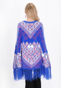 Poncho albastru cu un model geometric în nuanțe de roz și alb, având franjuri lungi la margine. Fabricat dintr-un material moale și pufos.