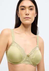 Heleheline rinnahoidja pitsilise detailiga tassis, keskel paelaga aksent ja reguleeritavad rihmad. Sile materjal poolmatt viimistlusega.