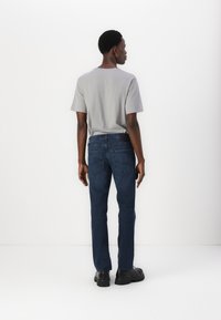 Gray short-sleeve t-shirt paired with dark blue denim jeans. The jeans feature a classic cut and two back pockets, and the outfit is complemented by black shoes.
