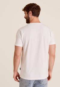 Witte katoenen t-shirt met korte mouwen en een ronde hals. De achterkant heeft een minimalistisch ontwerp en een klein label aan de zoom.