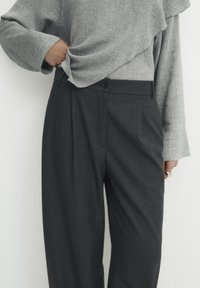 Grijze textuur top met ruches, gecombineerd met donkergrijze gestreepte broek met knoopsluiting en zijzakken.