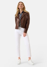 Bruine leren motorjack met een strak ontwerp, rits aan de voorkant en zijzakken, gecombineerd met een gestreepte polo en witte jeans.