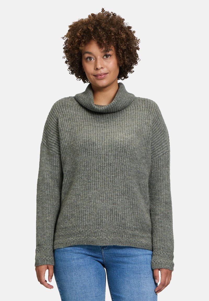 Grüner Strickpullover mit hohem Kragen, gerippter Textur, überschnittenen Schultern und langen Ärmeln, kombiniert mit blauen Denim-Jeans.