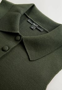 Mørkegrøn strikket polo-top med tekstureret stof, en klassisk krave og to knapdetaljer, mærket "NEXT" på etiketten.