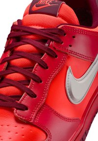 Rød Nike sneaker med syntetiske og lædermaterialer, tekstureret stoflynlås, vinrøde snørebånd og et sølvfarvet swoosh-logo.