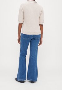 Pull en maille beige clair à manches courtes avec col, associé à un jean bleu évasé avec un design à cinq poches et des bords ourlés.