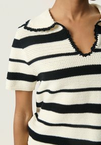Gebreid top met zwart-witte horizontale strepen, een gegolfde kraag en korte mouwen met ribbels. Textuur in de stofafwerking.