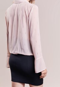 Helle rosafarbene, durchsichtige Bluse mit vertikalen Ausschnitten, langen Ärmeln und Kragen, kombiniert mit einem figurbetonten schwarzen Rock. Glatte Textur, elegantes Design.