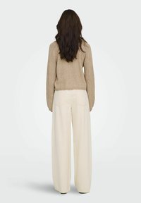 Pull en maille beige avec manches texturées, associé à un pantalon large crème. Le pull présente des poignets côtelés et une silhouette courte.