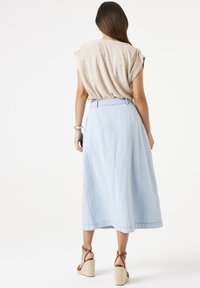 Lichtblauwe denimrok met een volle silhouet, een ceintuur in de taille en een zoom die onder de knie valt. Draag het met een beige top en een paar bruin leren wedges met bandjes.